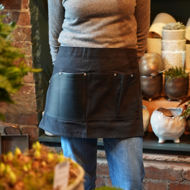 Female florist wearing handcrafted, black canvas waist (half)-apron; made in Britain with leather pocket.
