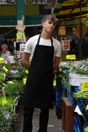 Man in a market wearing handcrafted black canvas apron with black straps: made in Britain.