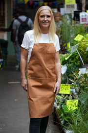 Lady in a market wearing handcrafted tan canvas apron with white straps: made in Britain.