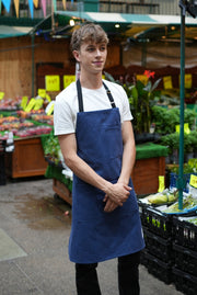 Man in a market wearing handcrafted blue canvas apron with black straps: made in Britain.