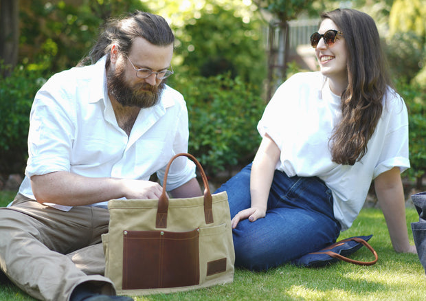 A man and a woman using a tan canvas gardening bag with leather handles and pockets