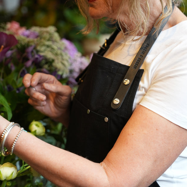 Female florist wearing handcrafted, black canvas apron; made in Britain with removable straps.