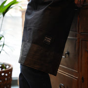 Close up of a handcrafted, black canvas apron; made in Britain with removable straps and leather trim.