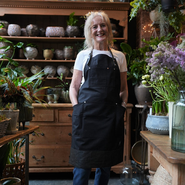 Female florist wearing handcrafted, black canvas apron; made in Britain with removable straps and leather trim.