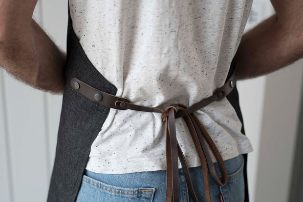 Handcrafted, black denim apron; made in Britain with pockets and removable leather straps.