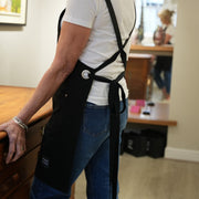 Female artist wearing a handcrafted, black canvas apron; made in Britain with removable straps.