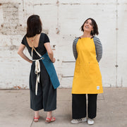 two people wearing canvas aprons with removable leather straps