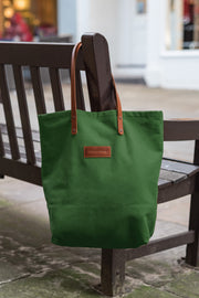 A handcrafted green canvas totebag hanging on a chair with leather straps.