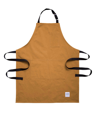 Handcrafted, tan canvas apron with black straps; made in Britain.